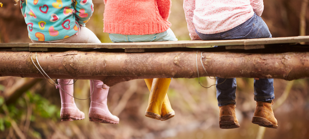 Children in rubber boots sitting on a tree trunk