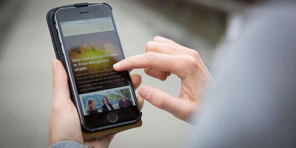 Studierender hält ein Smartphone in der Hand